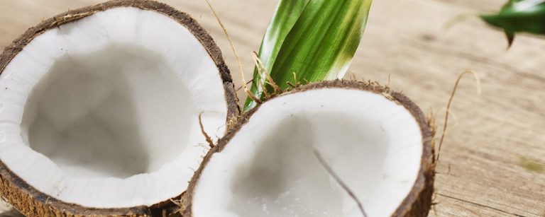 Eine Kokosnuss geöffnet auf einem Holztisch mit einem Blatt.
