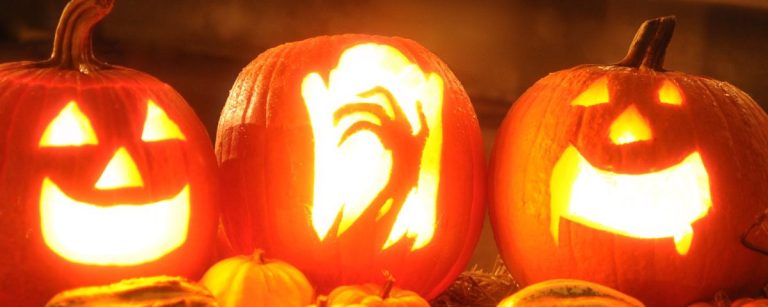 Beleuchtete Halloween-Kürbisse mit Gesichtern und kleineren Kürbissen im Vordergrund.