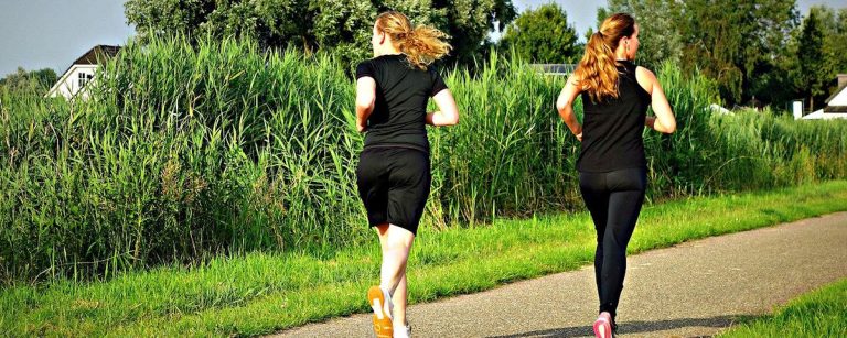 Zwei Frauen joggen auf einem Feldweg, umgeben von üppigem Grün, für ein Fitness- und Ernährungsunternehmen.
