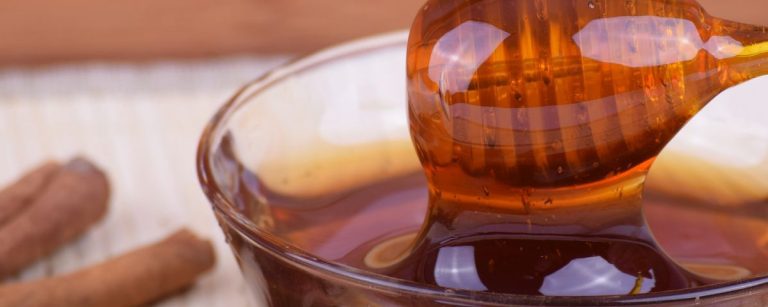 Goldener Honig fließt von einem Löffel in eine Schüssel, daneben Zimtstangen – perfekt für Fitness-Rezepte.