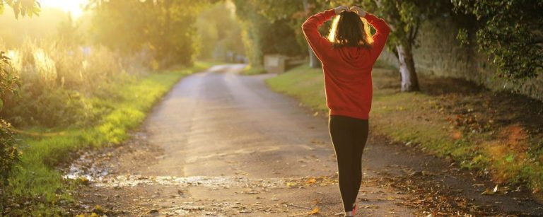 Junge Frau in rotem Hoodie joggt im goldenen Sonnenlicht auf einer Landstraße.