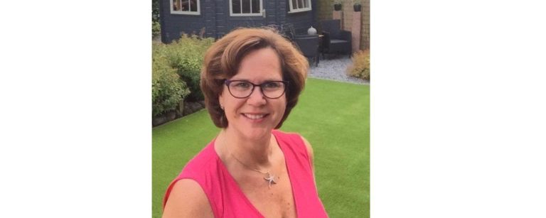 Frau mit Brille und pinkfarbenem Oberteil, lächelnd im Garten – ideal für Fitness- und Ernährungsblogs.