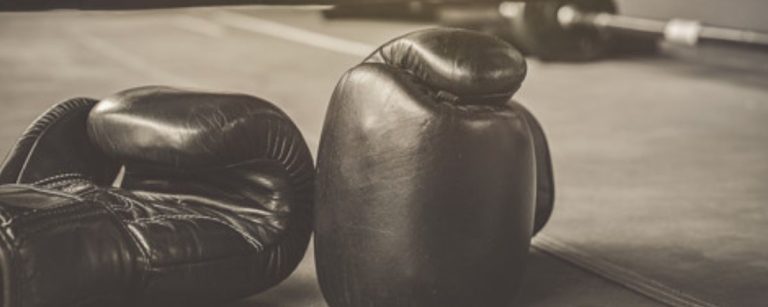 Schwarze Boxhandschuhe liegen auf einem Boxring.