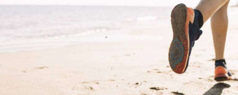 Ein Läufer in Turnschuhen und Shorts läuft am Strand entlang, um fit zu bleiben.