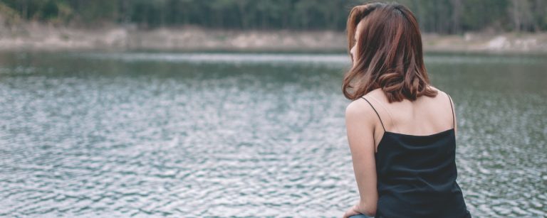 Junge Frau sitzt am Wasser in schwarzem Top.