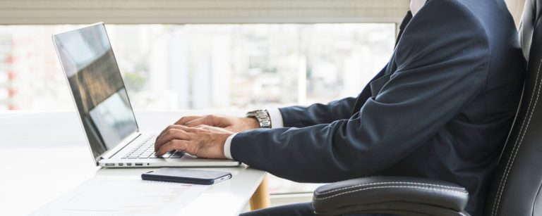 Mann im Anzug tippt auf Laptop, neben einer Schere im Behälter.
