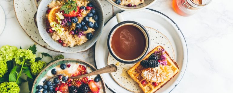 Gesunde Frühstücksschüssel mit Obst, Haferflocken, Beeren, Waffeln und Kaffee.
