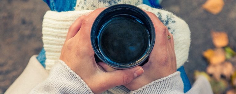 Hände halten eine Thermoskanne mit heißem Getränk, umgeben von Herbstlaub, ideal für Fitness-Ernährung.