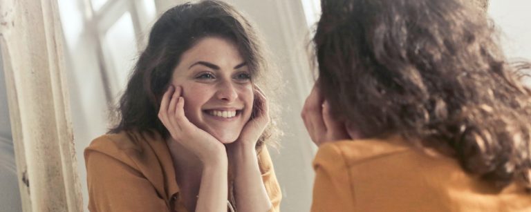 Frau lächelt sich im Spiegel an, motiviert für Fitness und gesunde Ernährung.
