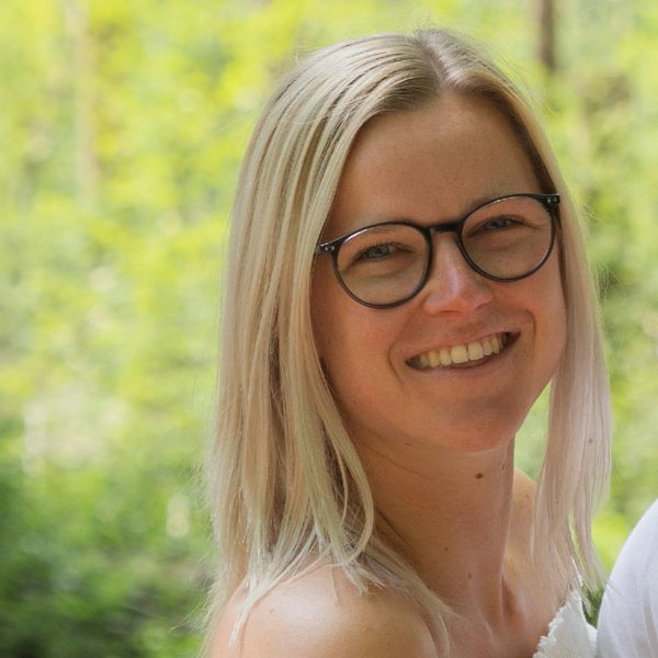 Blonde Frau mit Brille im Freien, lächelnd, für ein Fitness-Ernährungsunternehmen.