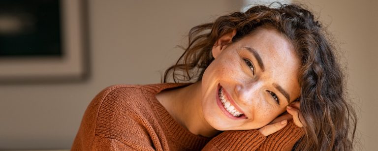 Lächelnde Frau mit Sommersprossen in orangefarbenem Pullover – Fitness und gesunde Ernährung.