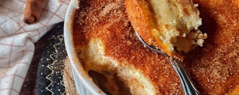 Slice of pear churro cheesecake with glossy caramelised pear wedges on top and a cinnamon-sugar crumb edge on a white plate.