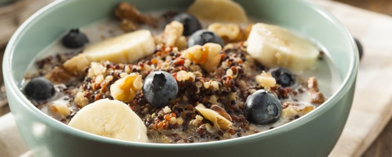 Colorful quinoa breakfast bowl topped with yogurt, fresh berries, nuts and seeds on a bright morning table.