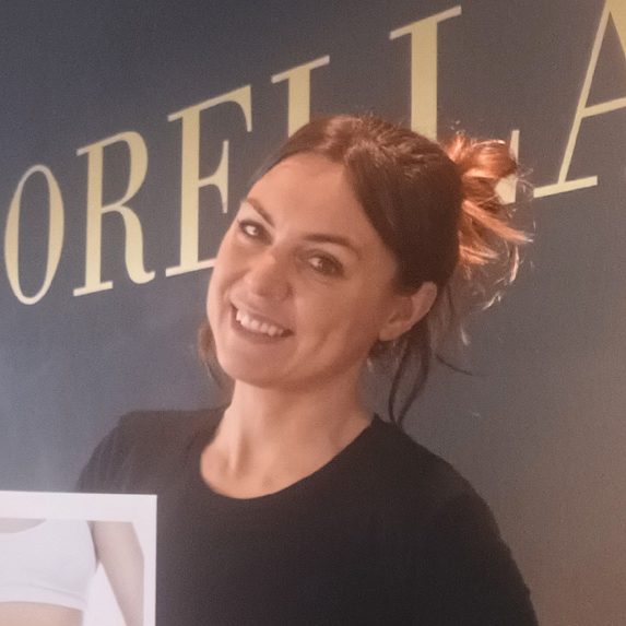 Frau lächelt vor blauem Hintergrund mit goldenem Schriftzug "SORELLA".