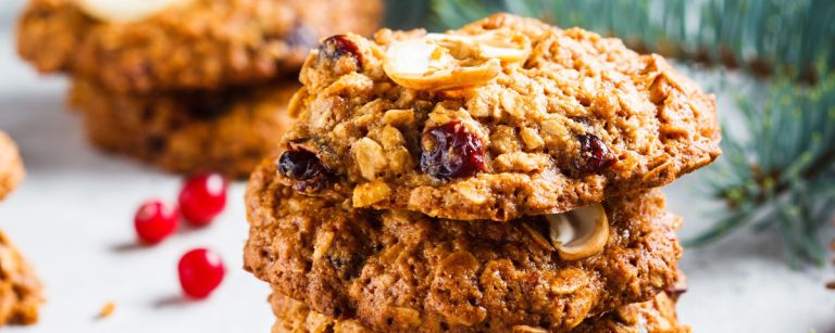 A stack of golden-brown oatmeal Christmas cookies with cranberries and chopped nuts, placed on a festive baking sheet.